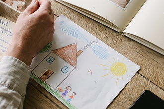 Kindertekening van een huis, zon en gezin naast een boekje